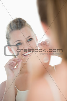 Cute woman using dental floss in front of mirror