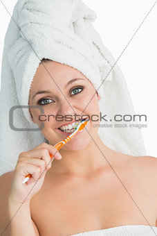 Smiling woman with hair towel washing her teeth