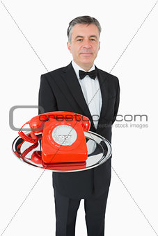 Well-dressed waiter holding a phone on a silver tray