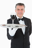 Cheerful waiter holding a glass of wine on a silver tray