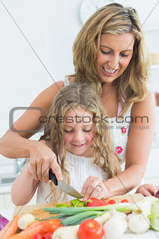 Mother teaching her daughter cutting vegetables