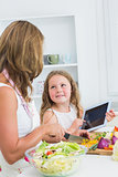 Mother cutting vegetables with her daughter using tablet