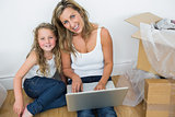Mother and daughter sitting on the floor and using laptop