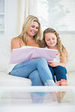 Smiling mother and daughter while reading book