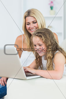 Mother and daughter sitting on the sofa with laptop
