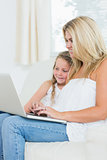 Woman typing on notebook while her daughter is sitting next to her