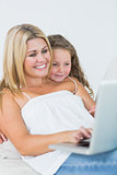 Mother using laptop with her daughter leaning on her shoulder