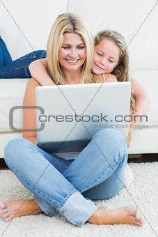 Mother sitting on the floor while her daughter hugging her from the sofa