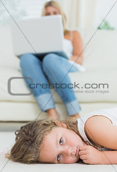 Daughter resting on the floor while her mother using notebook