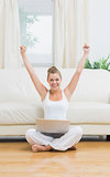 Cheerful woman raising hands while using laptop