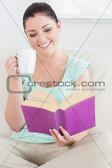 Woman sitting on the couch while reading and drinking