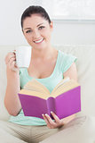 Woman sitting on the couch and reading while drinking