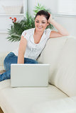 Woman sitting on the couch and smiling while using a laptop
