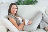 smiling woman lying on the sofa and holding a mug