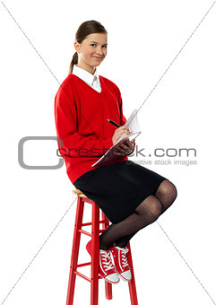 Girl sitting on high stool writing in notebook