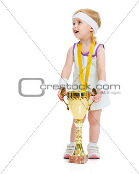 Happy baby in tennis clothes with medal and goblet looking on co