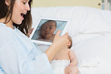 Smiling mother using a tablet to take a picture of a newborn baby