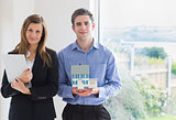 Estate agent holding clipboard and man holding miniature model house