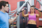 Trainer helping woman on weights machine