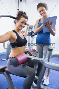 Happy female trainer and client on weights machine