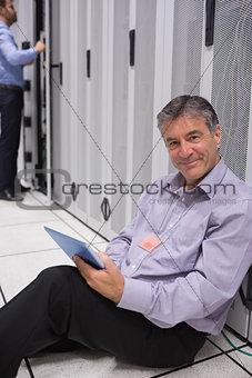 Smiling man sitting on the floor with his tablet beside servers