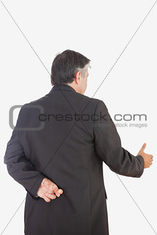 Mature businessman with fingers crossed offering handshake