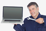 Mature mechanic holding wrench and laptop