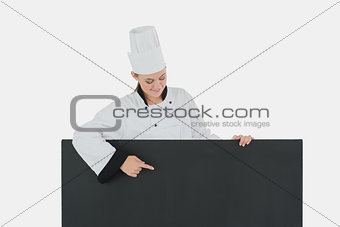 Woman in chef clothing points at black billboard