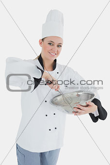Happy female chef holding wire whisk and mixing bowl
