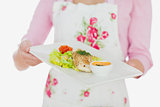 Woman in apron holding plate of healthy meal
