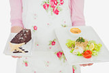 Maid holding plates of healthy meal and pastry