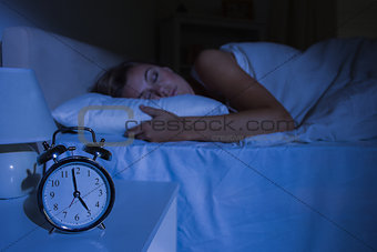 Focus on the alarm clock in front of sleeping woman