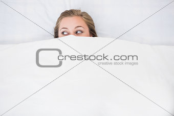 Blonde woman hiding under the duvet