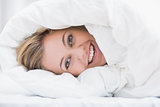 Happy woman hiding under the duvet
