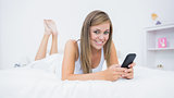 Happy woman lying on the bed with her phone