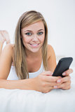 Smiling woman lying on the bed with her phone