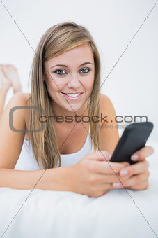 Smiling woman lying on the bed with her phone
