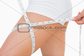 Midsection of woman measuring thigh