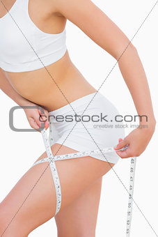 Slim woman measuring thigh with tape measure