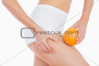 Woman squeezing fat on thigh as she holds orange