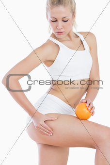 Attractive woman checking out fat on thigh as she holds orange