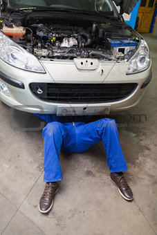 Male mechanic lying under car