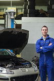 Happy mechanic standing by car with open hood