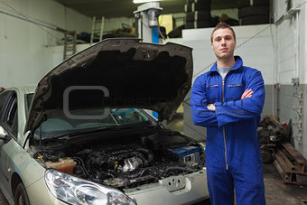 Confident auto mechanic by car