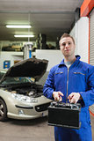 Confident auto mechanic with car battery