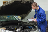 Mechanic with clipboard examining car engine