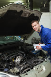 Auto mechanic with clipboard examining car