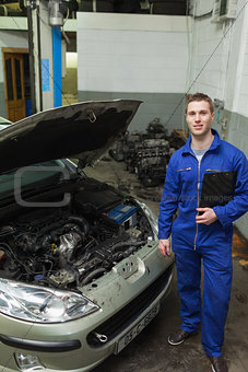 Confident mechanic standing by car with open hood