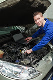 Happy mechanic with laptop repairing car