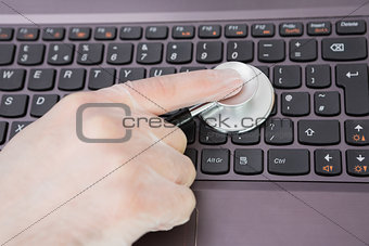 Hand examining laptop keyboard with stethoscope